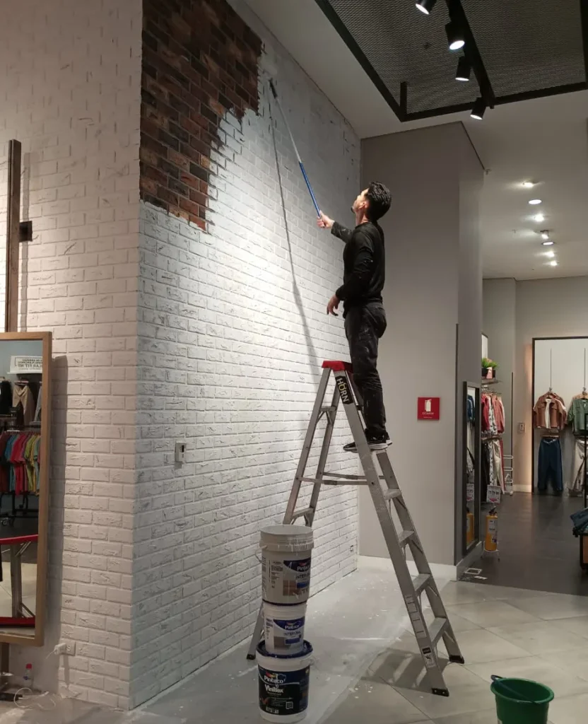 Técnico de Soluciones Azur pintando muro con textura de ladrillo en una tienda de moda en Medellín